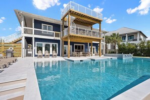 A two-story house with a swimming pool, outdoor seating, and a covered deck area.