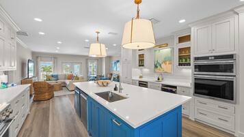 Une cuisine spacieuse avec des meubles blancs, des touches de bleu, un grand îlot central et des appareils électroménagers modernes.