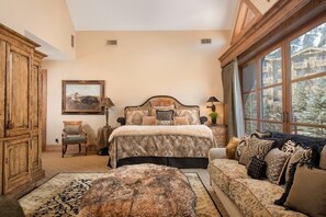 A bedroom with a large bed, a wooden wardrobe, a chair, a sofa, and a window with a view of trees. - Four Bedroom Penthouse in Teton Village (Teton Village)