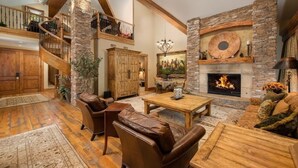 A spacious living area with a fireplace, leather furniture, and a wooden staircase. - Four Bedroom Penthouse in Teton Village (Teton Village)