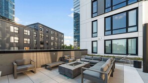 Eine Dachterrasse mit Außenmöbeln, einer Feuerstelle und Blick auf umliegende Gebäude.