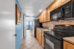 A kitchen with wooden cabinets, a black microwave, a stove, and a refrigerator. - The Caribbean Resort and Villa 1130 (Myrtle Beach)