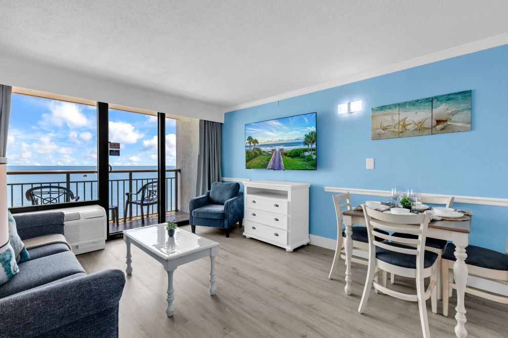 A living room with a balcony, a dining area, and a TV on the wall.