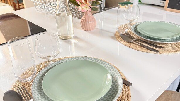 A clean, modern dining area with two sets of plates, cutlery, and glasses on woven placemats. A small vase with flowers adds a touch of color. - Le maréchal Deluxe T2 Tours centre-Nationale- Vieux tours (Tours)