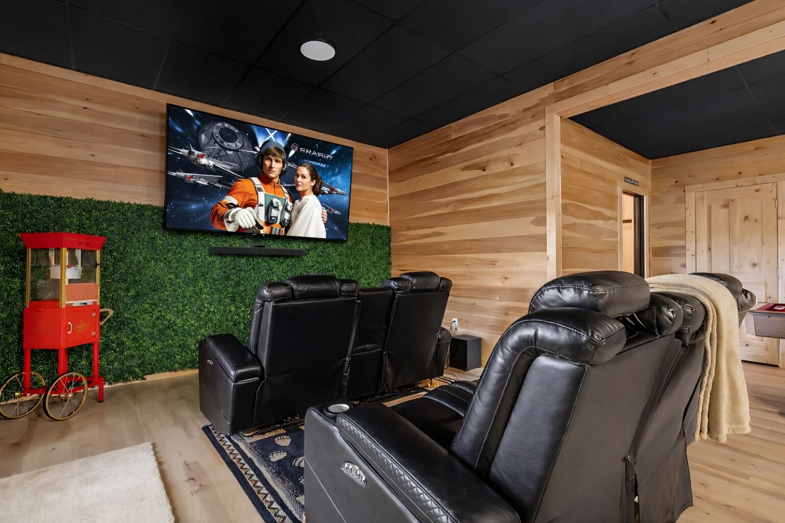 Une salle de cinéma privée avec un grand écran, des fauteuils inclinables en cuir noir et un chariot à pop-corn rouge.