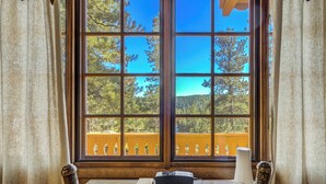 A room with a large window, a table with a vase, and a chair.