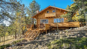 A wooden cabin with a balcony, a staircase, and a view of the surrounding forest.