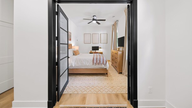 Une chambre à coucher comprenant un lit, des tables de chevet, une commode, un ventilateur de plafond et des tableaux encadrés accrochés au mur.