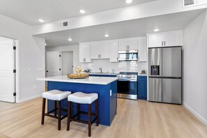 A modern kitchen with white cabinets, a blue island, stainless steel appliances, and wooden stools. - Brand New Arcadia 2 Bedroom & 2 Bath Apartment (Arcadia)