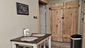 Un petit coin repas avec une table et des chaises, une porte en bois et une poubelle.