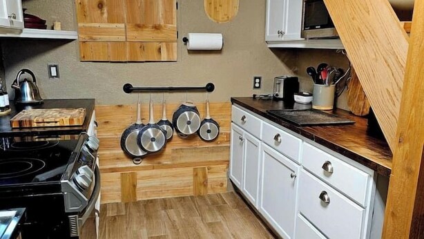 Une cuisine avec des meubles de rangement en bois, une cuisinière et des casseroles suspendues.