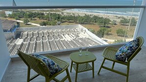 A balcony with two wicker chairs and a small table, overlooking a coastal area with a view of the sea and a distant shoreline. - Ocean view Building with 1 bedroom and AC in peaceful Cartagena de Indias (Cartagena de Indias)