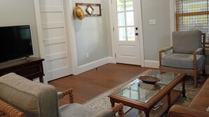 A living room with a television, two doors, a chair, a coffee table, and a window with blinds. - Walk to Historic St. Augustine | Guest Favorite (St. Augustine)