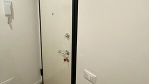Une porte fermée avec un cadre noir, un interphone fixé au mur et un interrupteur situé sur le mur adjacent.