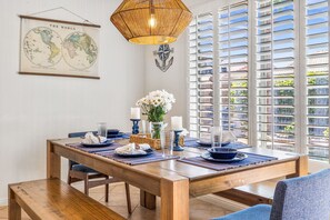 Un coin repas avec une table en bois dressée pour deux personnes, une carte du monde suspendue au mur et une ancre décorative.