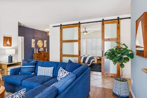 Un salon avec un canapé bleu, un meuble en bois, une plante en pot et une porte coulissante qui donne sur une autre pièce.