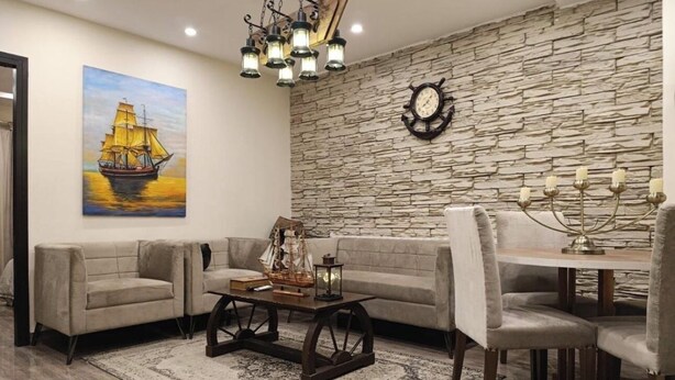 Un salon avec un mur en pierre, un tableau représentant un navire, une table basse en bois et un coin repas agrémenté d’un chandelier.