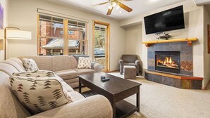 Un salon comprenant un canapé, des fauteuils, une table basse, une cheminée, un téléviseur et un ventilateur de plafond.