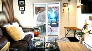 A living room with a leather sofa, a glass coffee table, and a view through a sliding glass door to an outdoor patio.