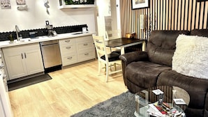 A modern kitchen with a dining area, a sofa, and a glass coffee table with magazines and remote controls.