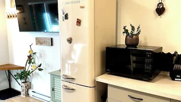 Een keuken met een witte koelkast, een magnetron, een klok en een kleine plant op het aanrecht.