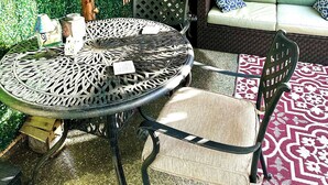An outdoor seating area with a round metal table, chairs, and a sofa with patterned cushions.