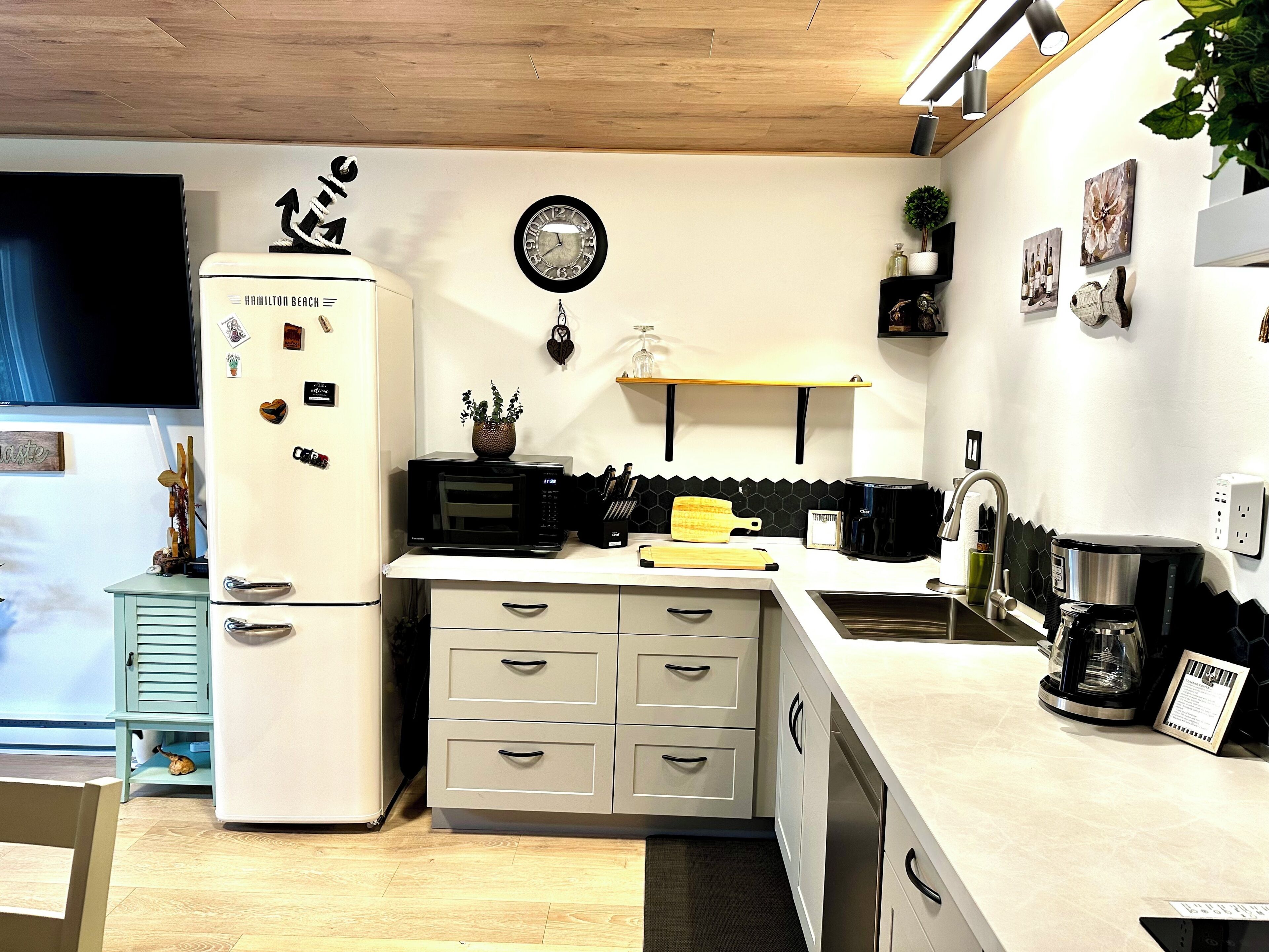 A compact kitchen with a refrigerator, microwave, sink, and a clock on the wall.