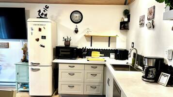 A compact kitchen with a refrigerator, microwave, sink, and a clock on the wall.