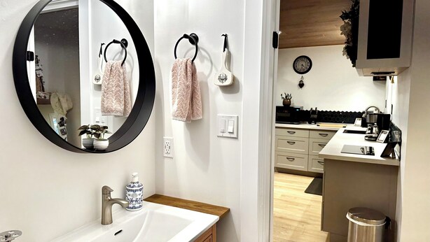 A modern bathroom with a round mirror, white sink, wooden cabinets, and a visible toilet.