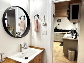 A modern bathroom with a round mirror, white sink, wooden cabinets, and a visible toilet. - Cozy 1-bedroom suite in charming Campbell River with private entrance & AC (Campbell River)
