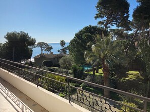 Balcón con vistas a un jardín ajardinado, una piscina y el mar.