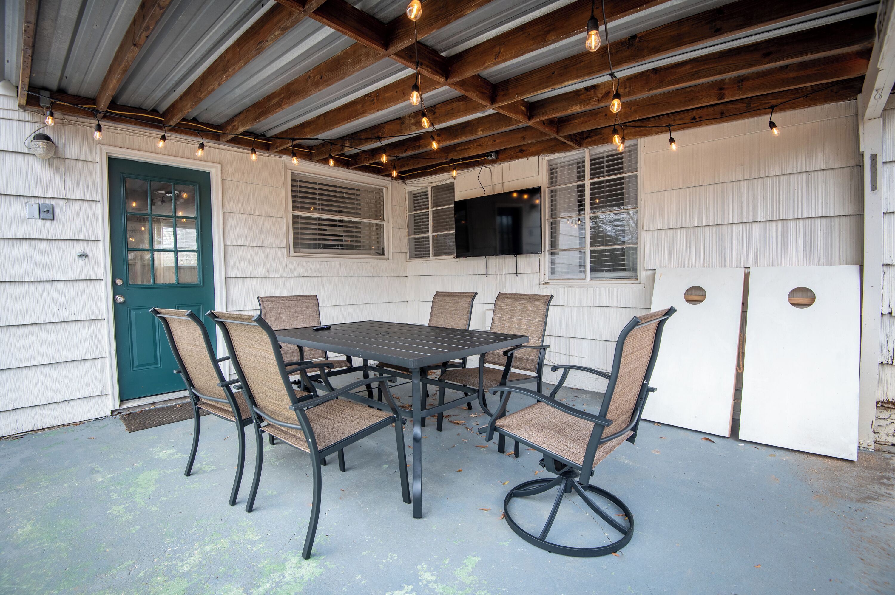 Eine Terrasse im Freien mit Tisch und Stühlen, einer grünen Tür und einem an der Wand befestigten Fernseher.