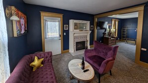 A living room with a fireplace, two purple armchairs, a coffee table, and a door with a window.