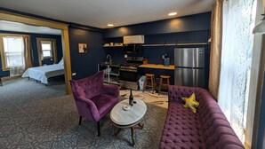 A compact living space with a bed, purple armchair, sofa, kitchen area, and a small dining table.