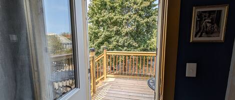A view from inside a room to an outdoor wooden deck with a railing, a framed picture on the wall, and a visible light switch.