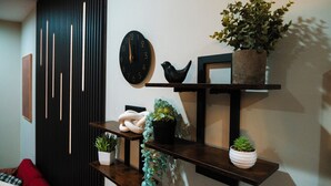 Una sala de estar moderna con un reloj negro, una escultura de pájaro negro y diversas plantas en macetas sobre estantes de madera.