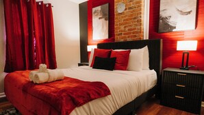Una habitación de hotel con una cama grande, cortinas rojas, una pared de ladrillo y obras de arte en las paredes.
