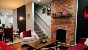 Una sala de estar con chimenea, muebles rojos y blancos, y una escalera que lleva a otra habitación.