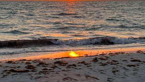 A beach with waves, a sunset, and a clear sky.