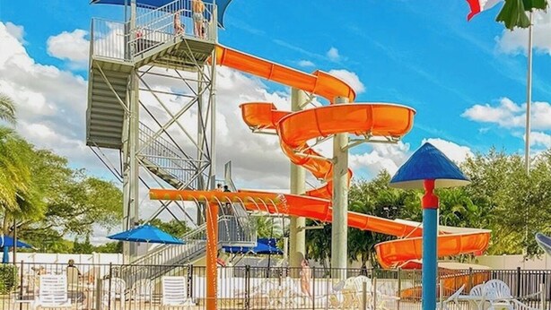 A water park with a tall water slide, a pool, and umbrellas.