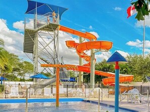 Ein Wasserpark mit einer hohen Wasserrutsche, einem Schwimmbecken und Sonnenschirmen.