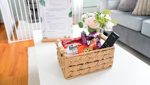 A wicker basket on a white table with snacks and a bouquet of flowers. - Cozy River Valley Family Retreat w/ Fireplace, Games & Serene Deck (Sparrow Bush)