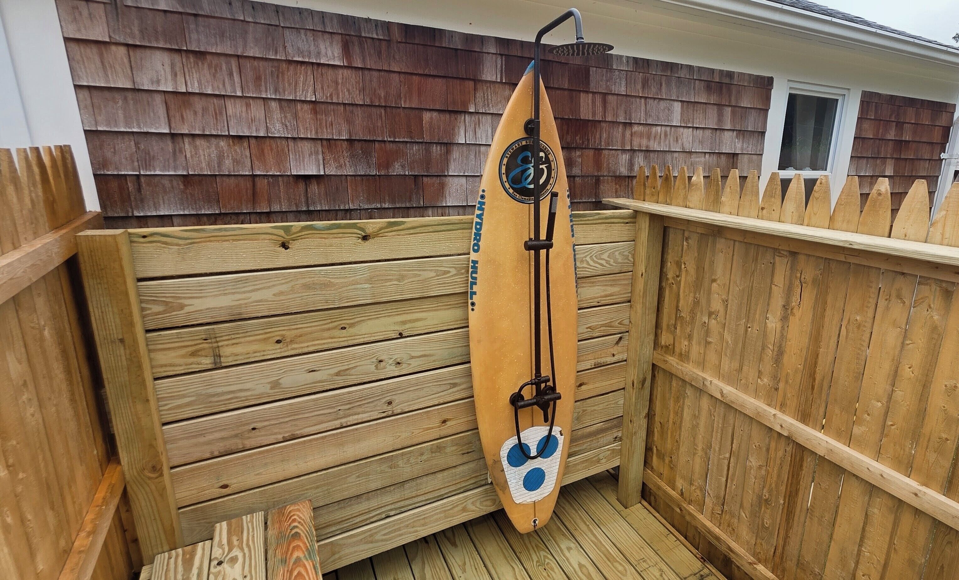 Eine Holzterrasse mit einem Surfbrett, das an einem Holzzaun angelehnt ist.