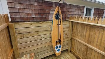 Eine Holzterrasse mit einem Surfbrett, das an einem Holzzaun angelehnt ist.