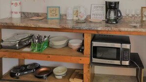 Une cuisine avec des meubles de rangement en bois, un plan de travail sur lequel on trouve divers ustensiles de cuisine, une machine à café et un four à micro-ondes.