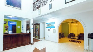 A hotel lobby with a reception desk, a green wall, a large painting, and a seating area with a yellow curtain. - Excelsa Lodge (Ejisu)