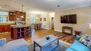 A modern kitchen with wooden cabinets, a dining area with a table and chairs, a living room with a sofa and a TV, and a hallway with a door. - Cozy Williston Retreat Near WEC, HITS and Local Springs-Perfect for Show Stays 🐴 (Williston)