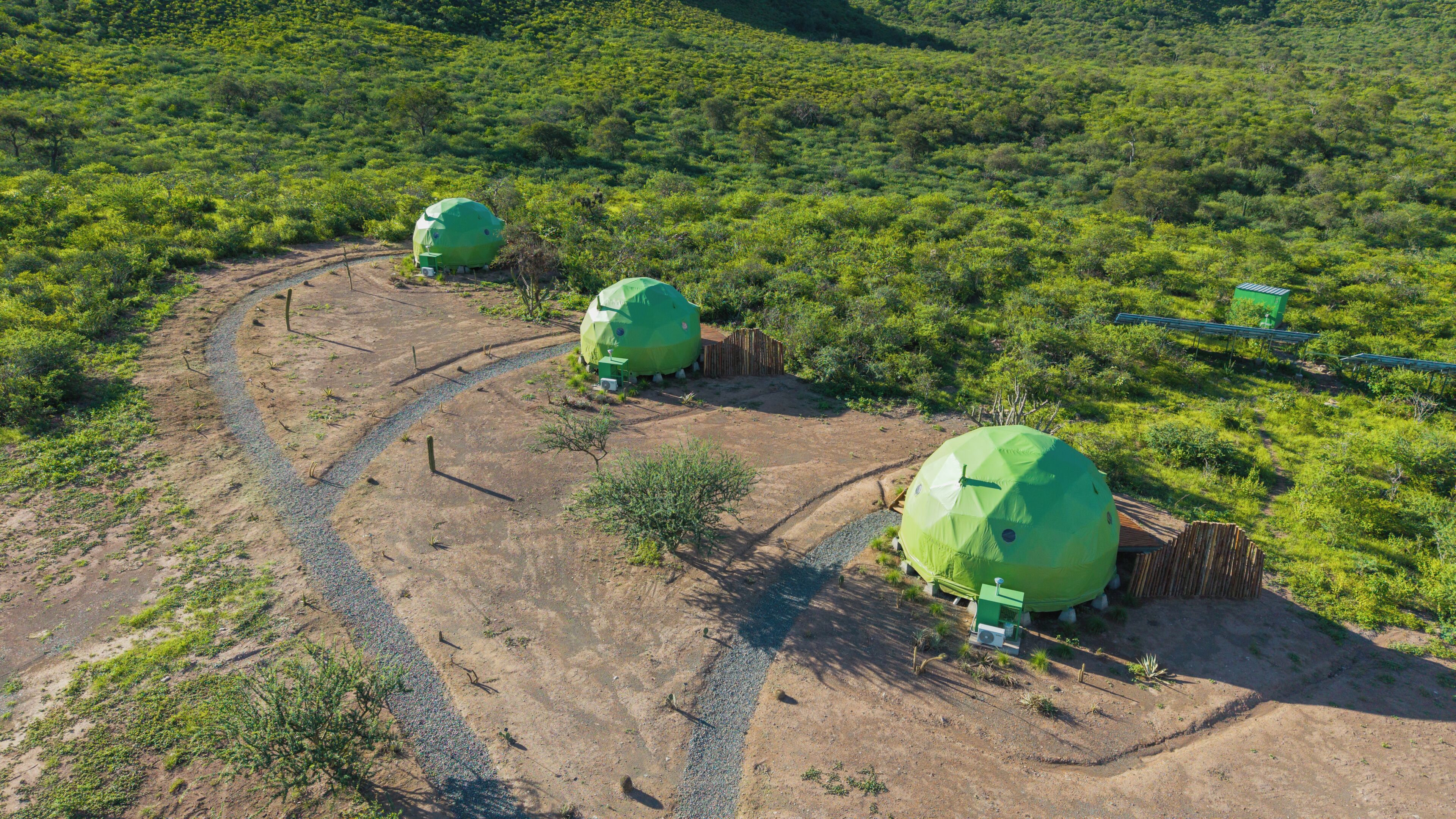 Three dome-shaped structures in a natural setting with a gravel path leading to them.