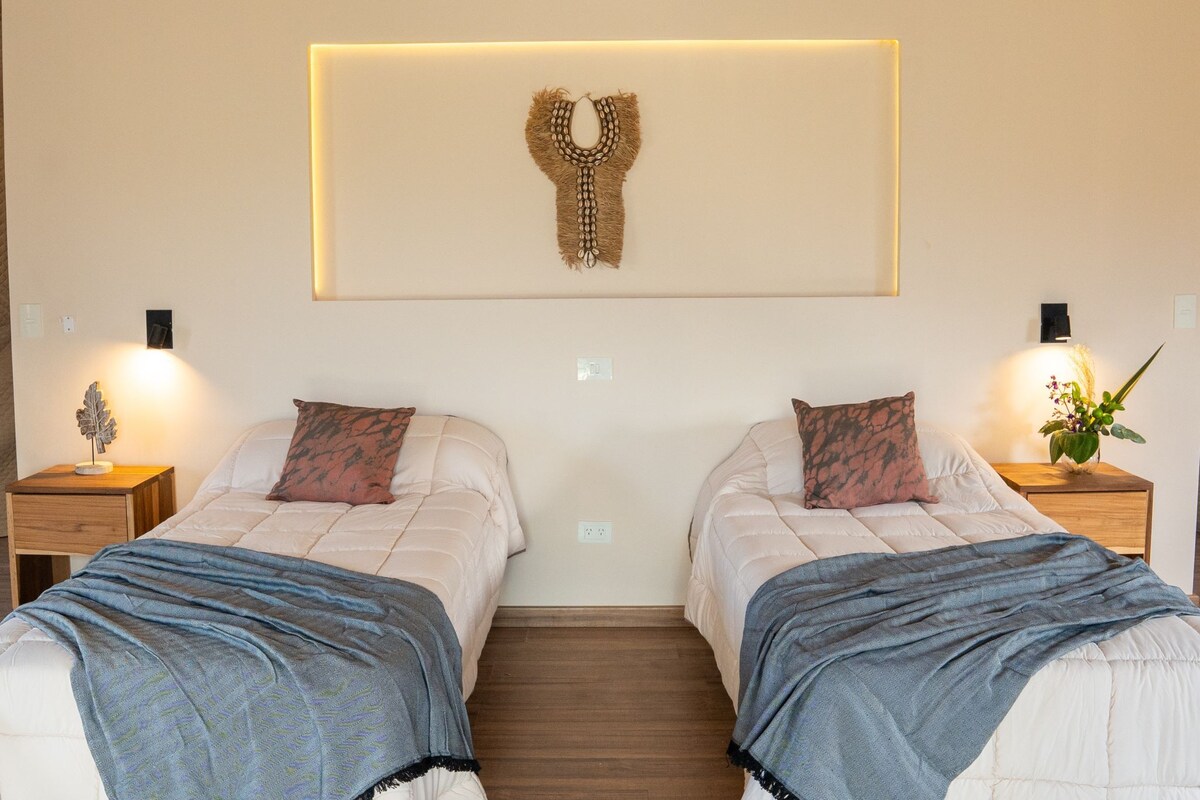 A double room with two beds, nightstands, wall-mounted artwork, and a small plant.