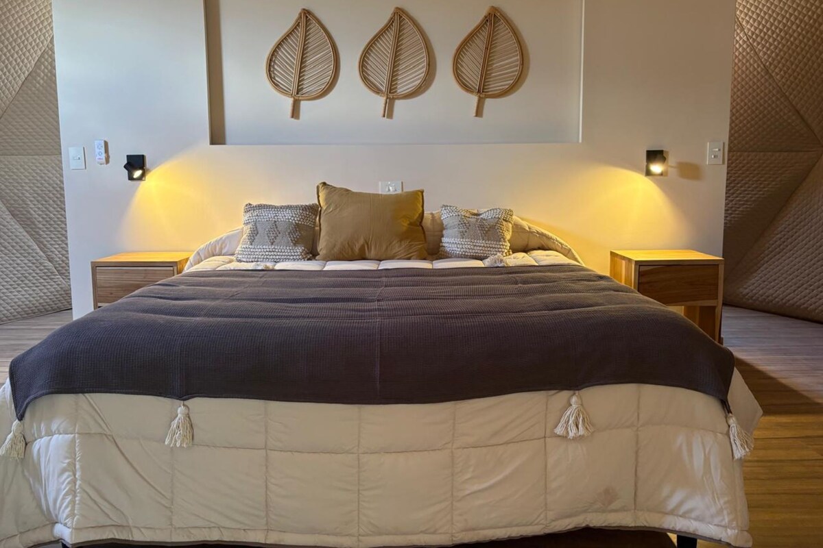 A bedroom with a large bed, two bedside tables, and three wall-mounted light fixtures.